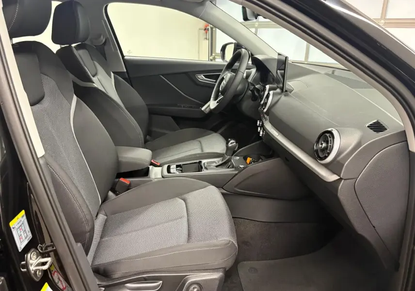 Vue intérieure côté gauche de l'Audi Q2 35 TFSI S Line 2026 en Noir Mythic, montrant sièges avant et tableau de bord.