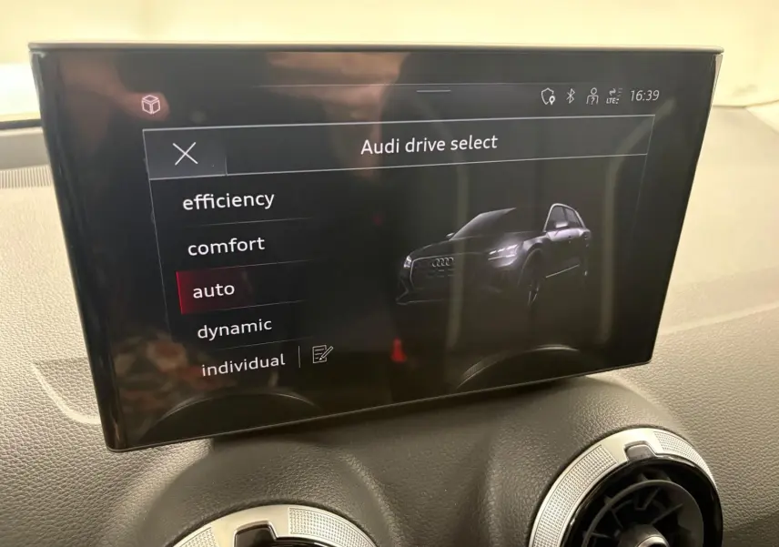 Écran central affichant le menu Audi drive select avec une illustration du SUV Audi Q2 noir Mythic en vue de face.