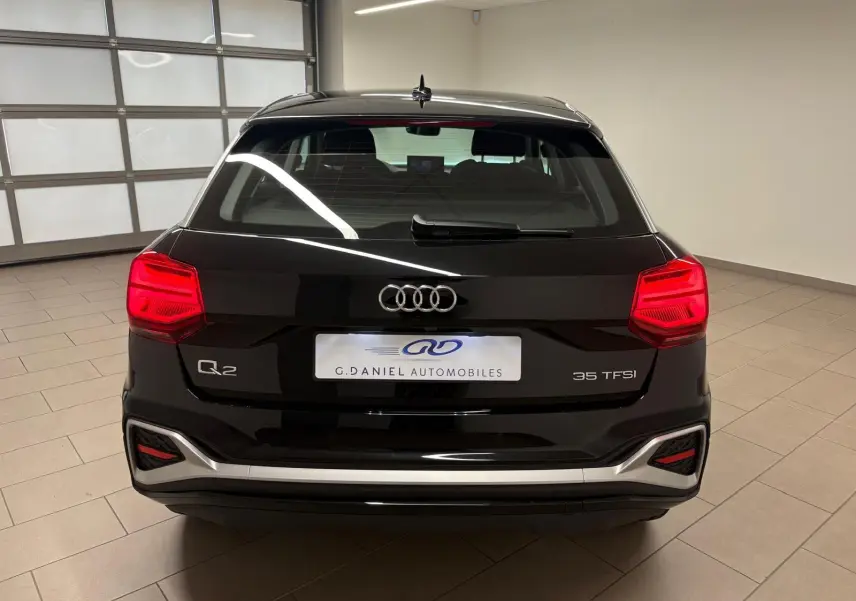Vue arrière d'un Audi Q2 35 TFSI noir Mythic avec feux rouges allumés dans un showroom intérieur.