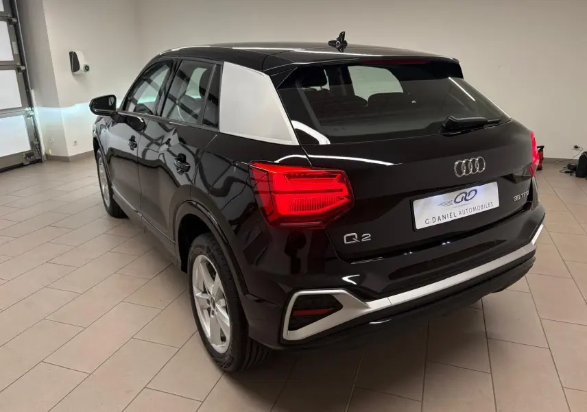Vue 3/4 arrière droite d'un Audi Q2 35 TFSI S Line noir Mythic avec inserts argentés et feux arrière allumés en intérieur.