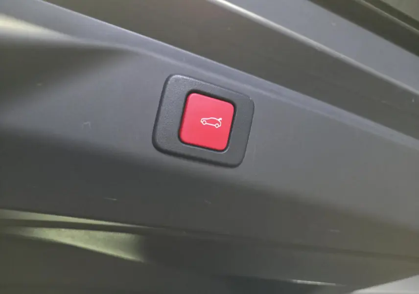 Bouton rouge d'ouverture électrique du hayon sur le bord intérieur d'un Peugeot 3008 noir hybride 2025.