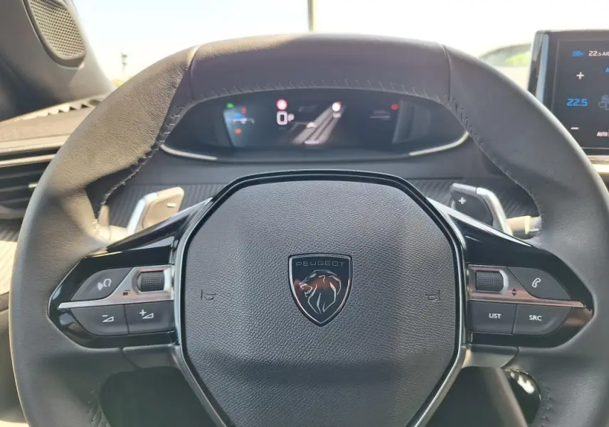 Vue rapprochée du volant noir de la Peugeot 2008 Hybrid 136 e-DCS6 Allure avec commandes intégrées et tableau de bord numérique.