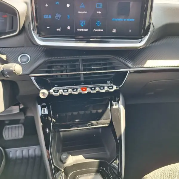 Vue intérieure centrée sur la console centrale et l'écran tactile du Peugeot 2008 Hybrid noir avec commandes piano et finition brillante.
