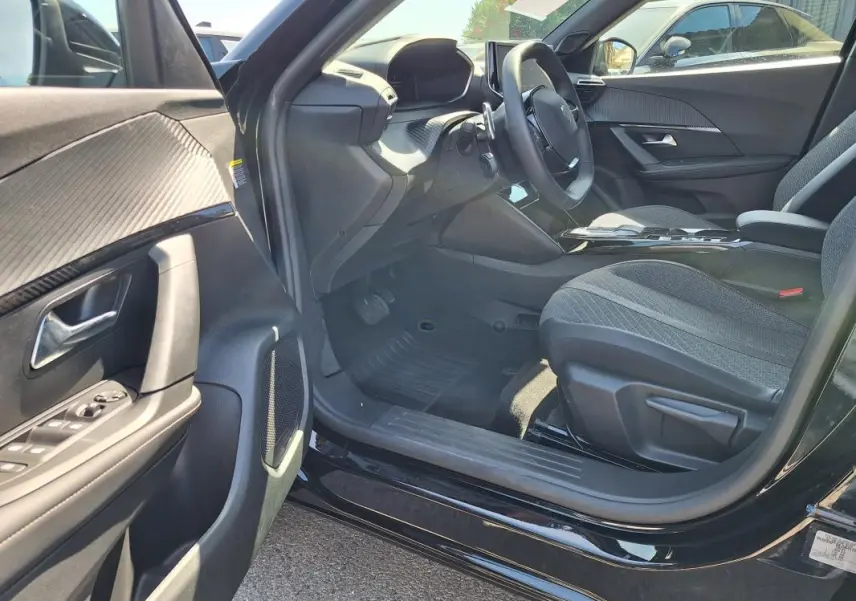 Vue intérieure côté conducteur de la Peugeot 2008 Hybrid noire, mettant en valeur le tableau de bord et les sièges tissu.