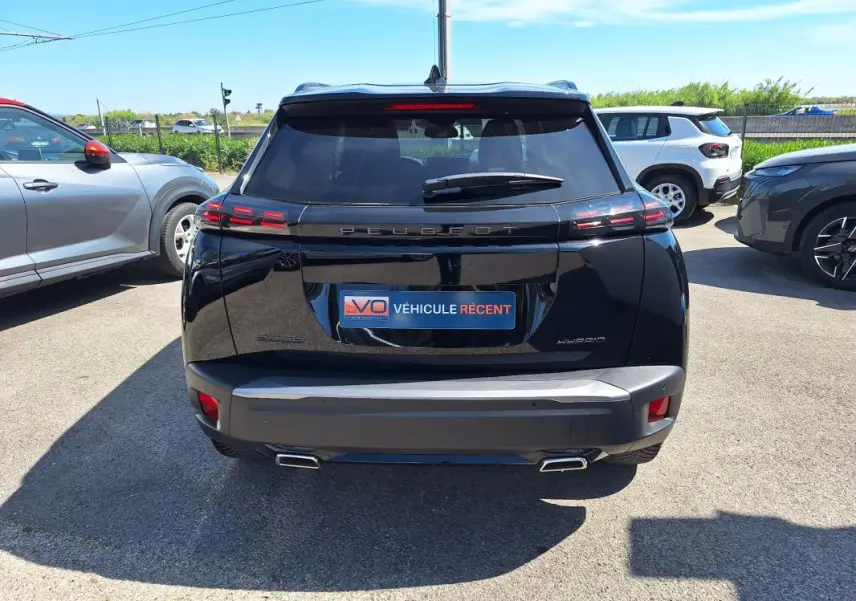 Vue arrière d’un Peugeot 2008 Hybrid noir 2025 avec barres de toit et jantes alliage 17 pouces, en extérieur.