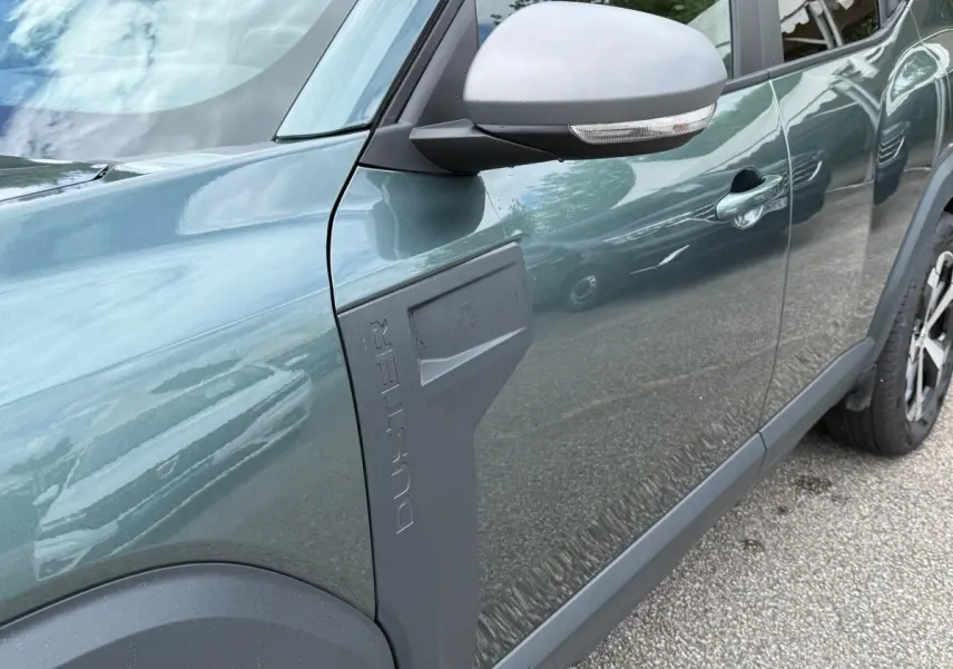 Vue latérale côté gauche du Dacia Duster Hybrid 140 Journey vert cèdre avec logo Duster en relief sur l'aile avant.