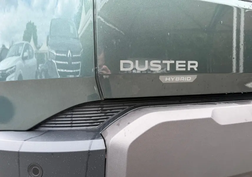 Gros plan sur l'arrière vert cèdre du Dacia Duster Hybrid avec logo et pare-chocs gris texturé.