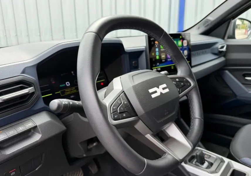 Vue intérieure rapprochée du volant multifonctions en cuir synthétique du Dacia Duster Hybrid 140 Journey 2025.