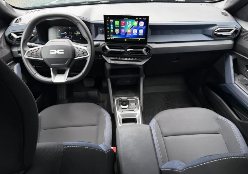 Vue intérieure avant du Dacia Duster Hybrid 140 Journey 2025, tableau de bord moderne avec écran tactile central et volant multifonctions.