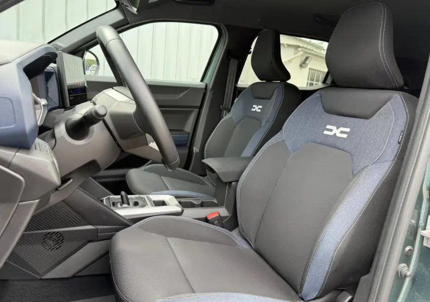 Vue intérieure côté conducteur du Dacia Duster Hybrid 140 Journey avec sièges bi-matière noirs et bleus et volant multifonctions.