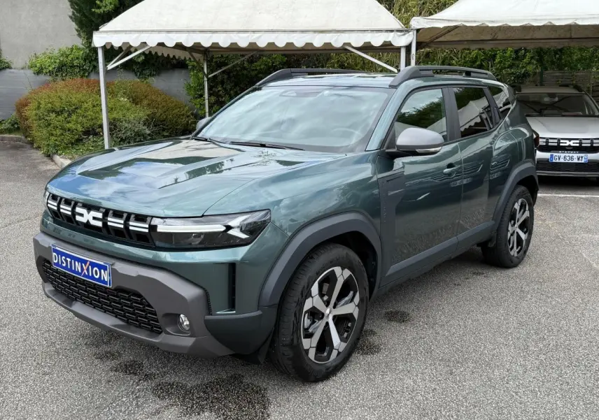 Dacia Duster Hybrid 140 Journey vert cèdre en 3/4 avant droit, avec jantes alliage et barres de toit noires.