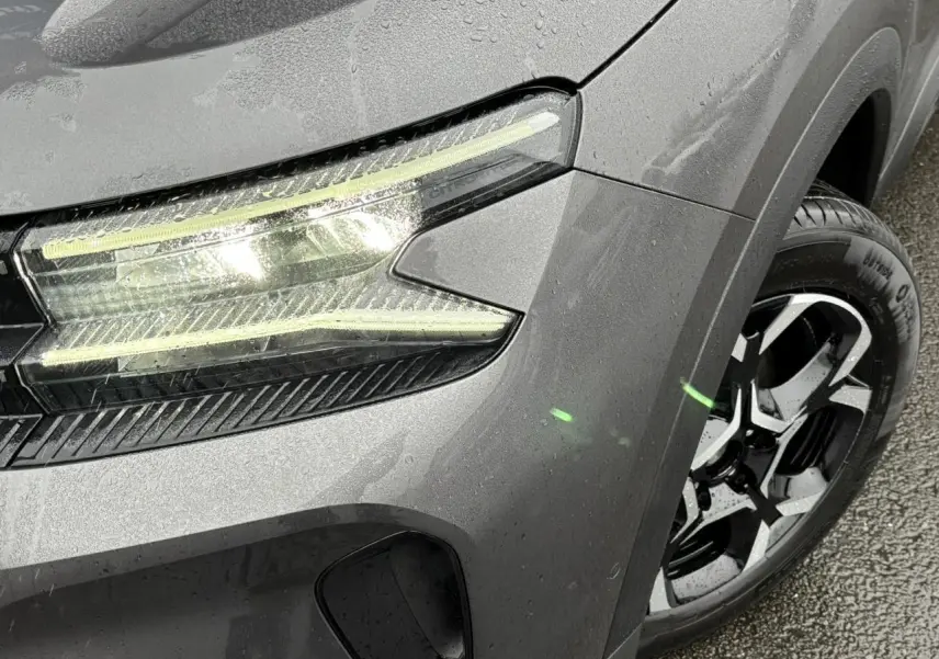 Gros plan sur le phare avant gauche allumé et la jante alliage bi-ton du Citroën C5 Aircross gris Platinium humide.