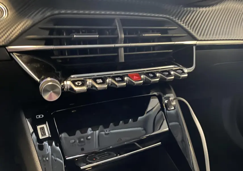 Vue rapprochée de la console centrale noire brillante du Peugeot 2008 e-136 Allure Pack avec boutons chromés et câble USB connecté.