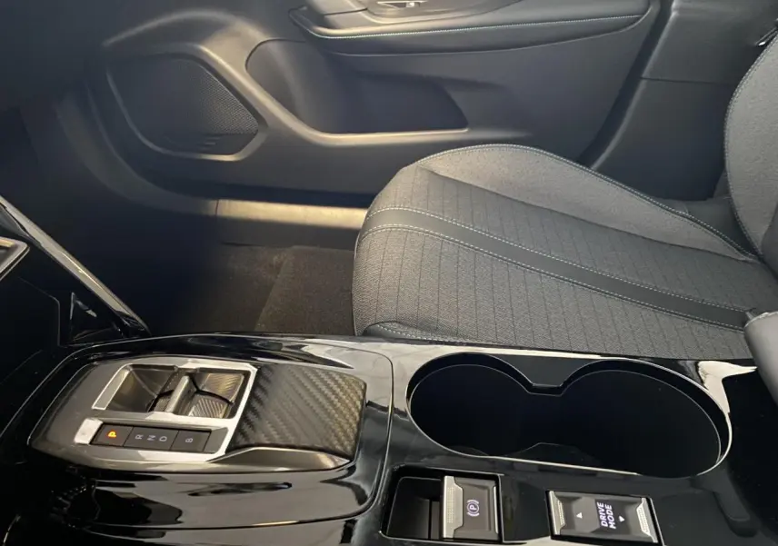 Gros plan sur la console centrale noire brillante et la sellerie tissu gris du siège avant droit du Peugeot 2008 e-136 Allure Pack.