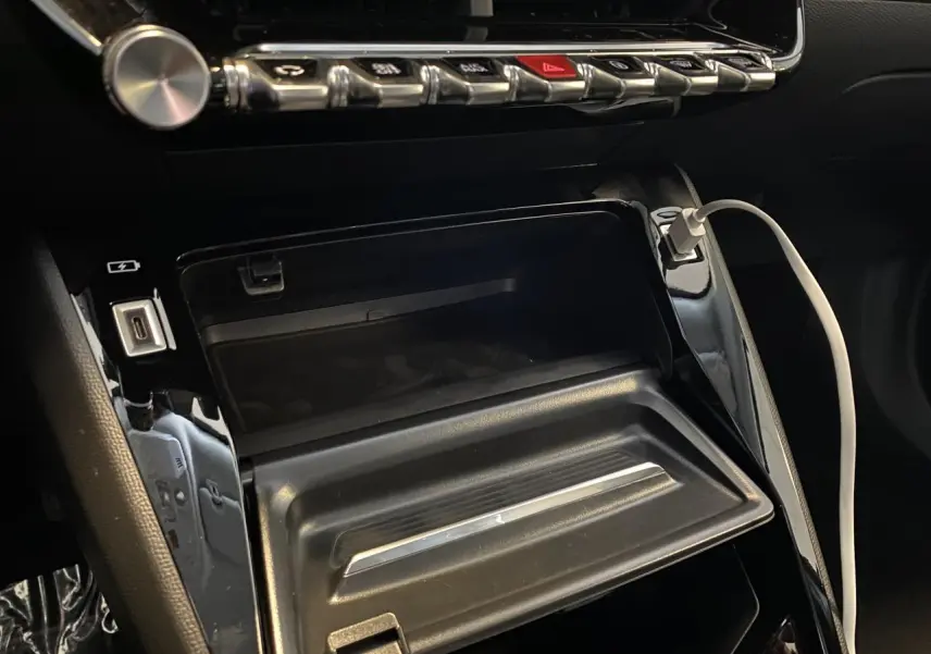 Gros plan sur la console centrale du Peugeot 2008 e-136 Allure Pack 2022 avec câble USB blanc connecté.