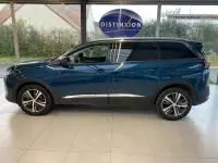 Profil côté gauche d’un Peugeot 5008 bleu célèbes 2022 avec jantes alu et barres de toit visibles en intérieur showroom.