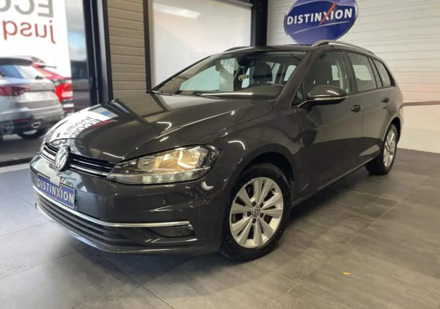 Volkswagen Golf SW gris foncé vue 3/4 avant droit en intérieur avec phares allumés et jantes alliage 16 pouces.