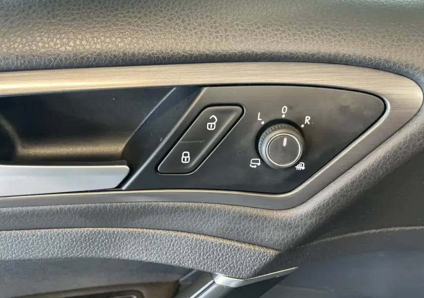 Détail de la commande de réglage des rétroviseurs et verrouillage sur la porte côté conducteur d'une Volkswagen Golf SW gris foncé.