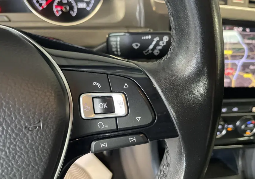 Gros plan sur les commandes gauche du volant cuir noir d'une Volkswagen Golf SW 1.6 TDI 2017 avec tableau de bord et écran tactile en arrière-plan.