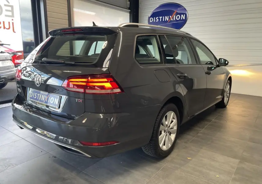 Volkswagen Golf SW gris foncé vue 3/4 arrière droit avec feux arrière allumés en intérieur showroom.