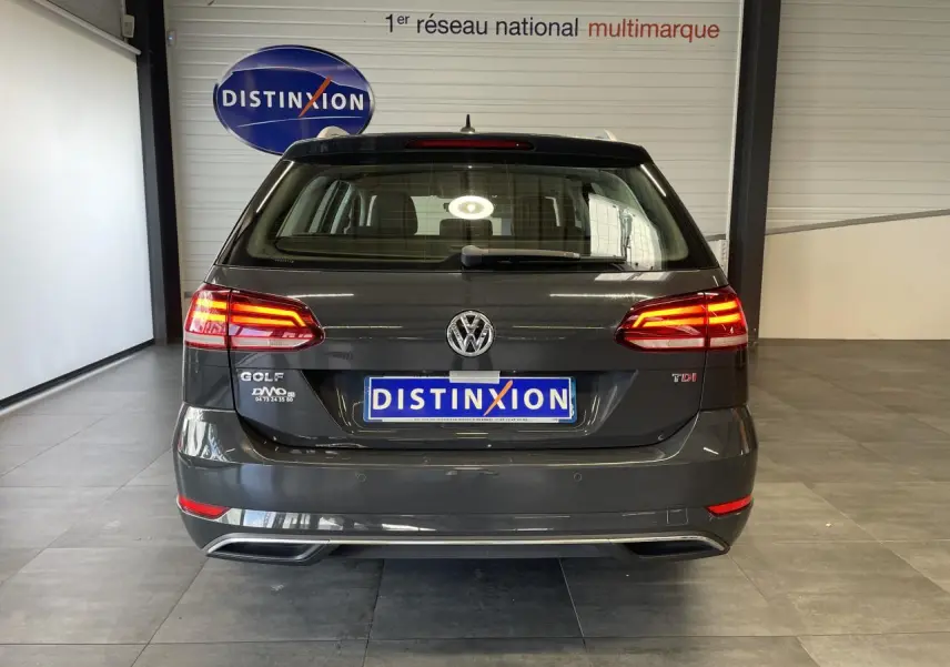 Vue arrière d'une Volkswagen Golf SW gris foncé avec feux allumés et logo Distinxion en intérieur showroom.