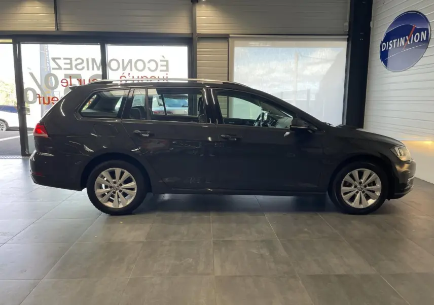 Profil côté gauche d'une Volkswagen Golf SW gris foncé 2017 avec jantes alliage et vitres teintées en intérieur showroom.