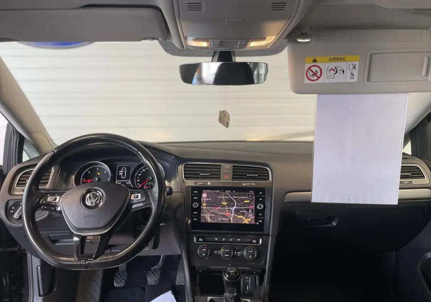 Vue frontale de l'intérieur noir de la Volkswagen Golf SW 2017, montrant le volant cuir et l'écran tactile central avec navigation.