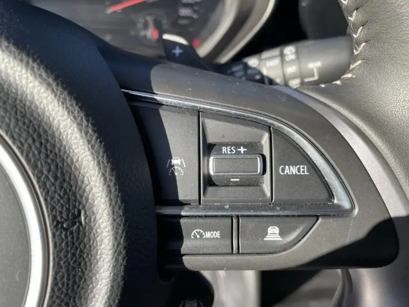 Gros plan sur les commandes noires du régulateur de vitesse au volant de la Suzuki Swift blanche 2025, côté droit.