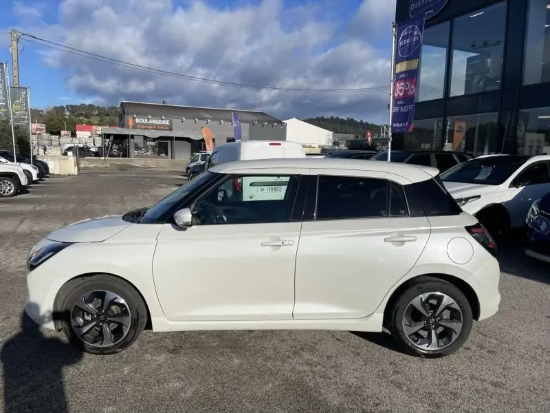 Vue de profil côté gauche d'une Suzuki Swift blanche 2025 avec toit noir et jantes alliage foncé, stationnée en extérieur.
