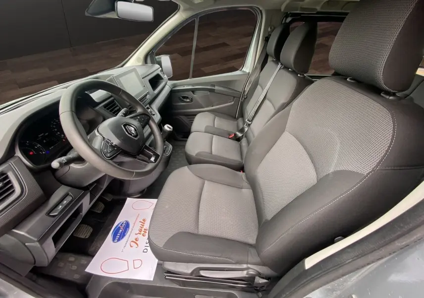Vue intérieure côté conducteur du Renault Trafic Combi gris platine 2023, montrant les sièges tissu noirs et le tableau de bord moderne.