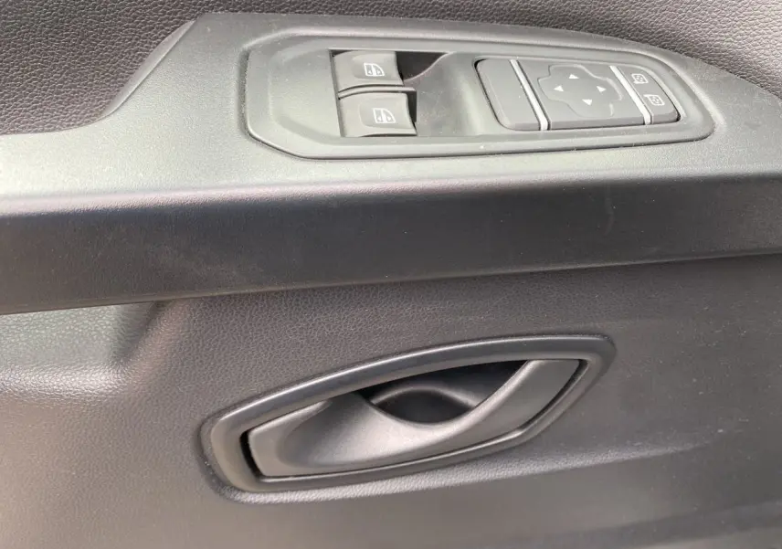 Gros plan sur la poignée intérieure et les commandes de lève-vitres côté conducteur du Renault Trafic Combi gris platine 2023.