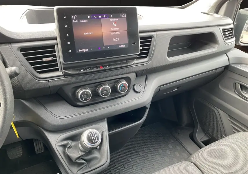 Vue intérieure côté passager du tableau de bord gris et de la console centrale avec écran tactile et levier de vitesses manuel.