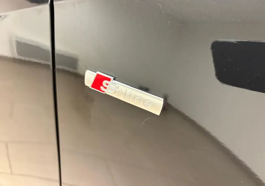 Gros plan sur l'emblème S line argent et rouge sur la porte latérale d'un Audi Q2 noir Mythic.