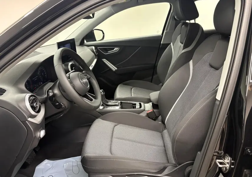 Vue intérieure côté conducteur de l'Audi Q2 35 TFSI S Line 2026 avec sièges tissu gris et tableau de bord noir.