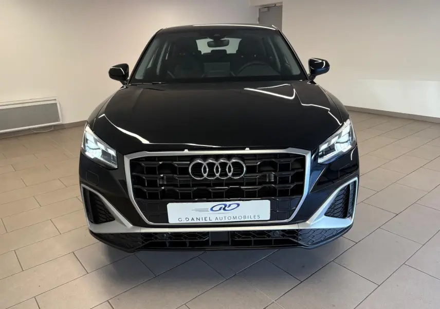 Vue frontale d'un Audi Q2 35 TFSI S Line noir mythic avec calandre hexagonale et phares LED allumés dans un showroom.