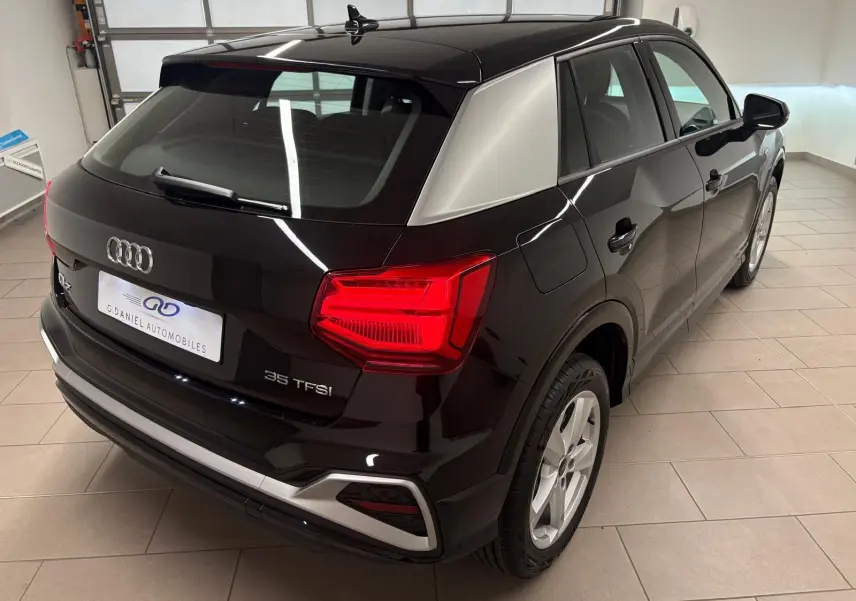 Audi Q2 35 TFSI S Line noir mythic vue 3/4 arrière droit en intérieur avec feux arrière allumés.