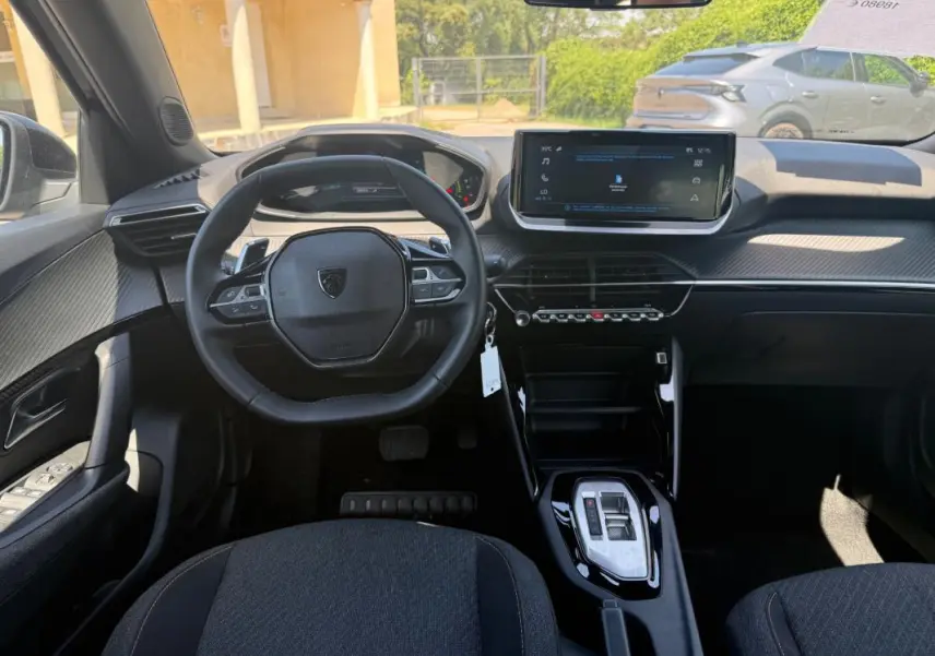 Vue intérieure frontale du poste de conduite du Peugeot 2008 Hybrid noir avec écran tactile et volant compact multifonction.