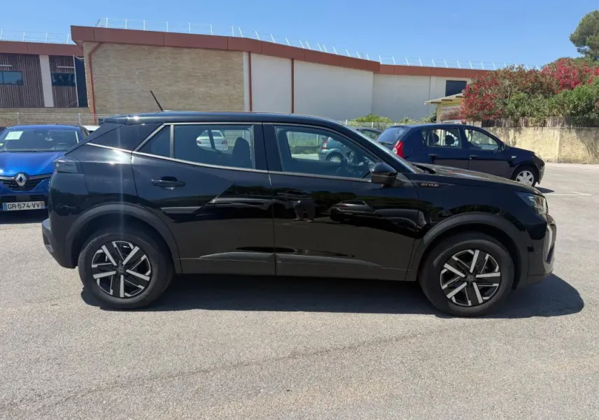 Profil côté gauche d’un Peugeot 2008 Hybrid 136 e-DCS6 Style noir avec jantes 16 pouces, en extérieur sur parking.