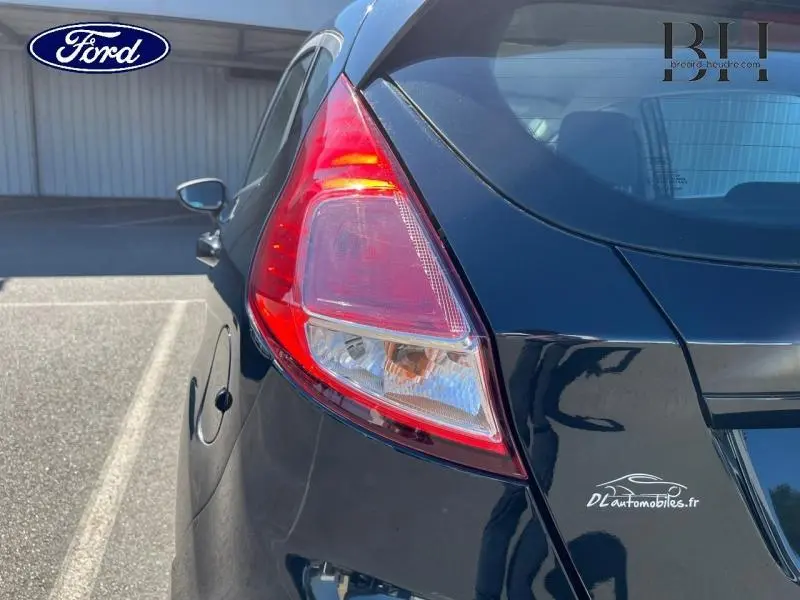 Vue arrière côté gauche d'une Ford Fiesta noire de 2015, mettant en valeur le feu arrière et la carrosserie brillante.