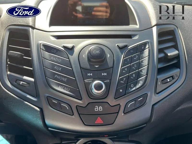 Vue rapprochée du tableau de bord central noir de la Ford Fiesta 2015 avec commandes audio et climatisation.