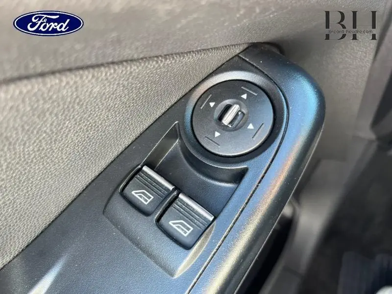 Gros plan sur les commandes de réglage des rétroviseurs et des vitres côté conducteur d’une Ford Fiesta noire de 2015.
