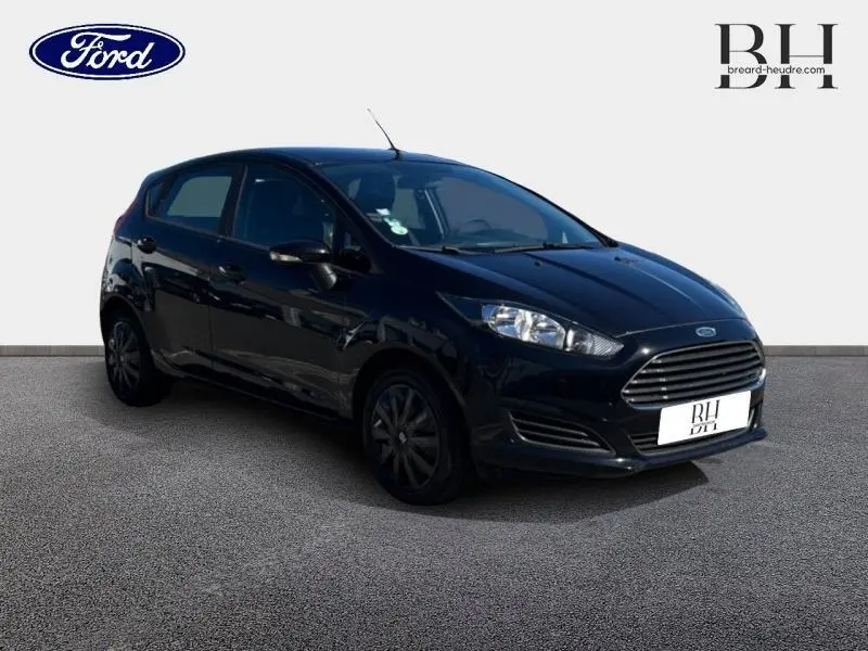 Vue 3/4 avant droit d'une Ford Fiesta noire 5 portes, avec calandre chromée et jantes foncées, sur fond neutre.