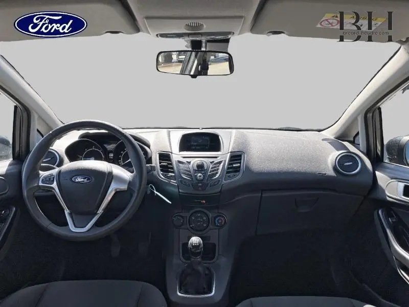 Vue intérieure avant du tableau de bord et volant de la Ford Fiesta noire 2015 avec boîte manuelle et commandes centrales visibles.