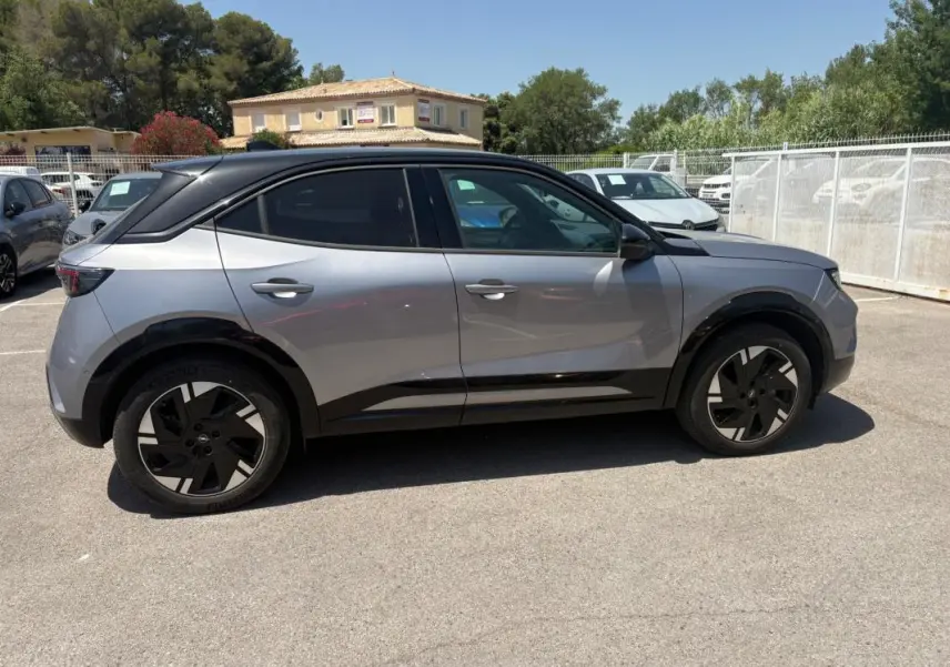 Vue de profil côté gauche d’un Opel Mokka électrique gris avec jantes alliage noires et vitres surteintées.