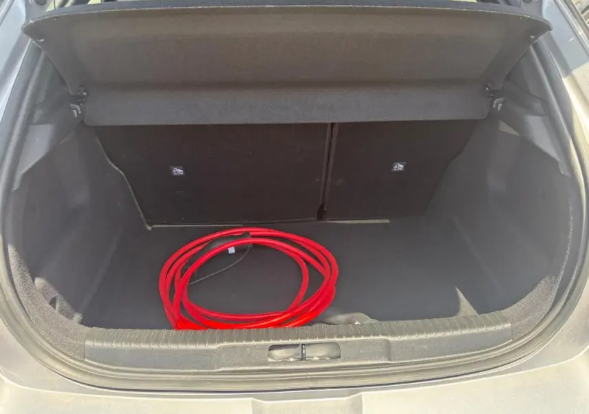 Coffre ouvert d’un Opel Mokka électrique gris, vue arrière, avec câble de recharge rouge visible à l’intérieur.