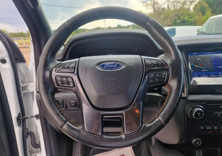 Vue intérieure centrée sur le volant en cuir noir du Ford Ranger Wildtrak blanc avec écran tactile et commandes au volant visibles.