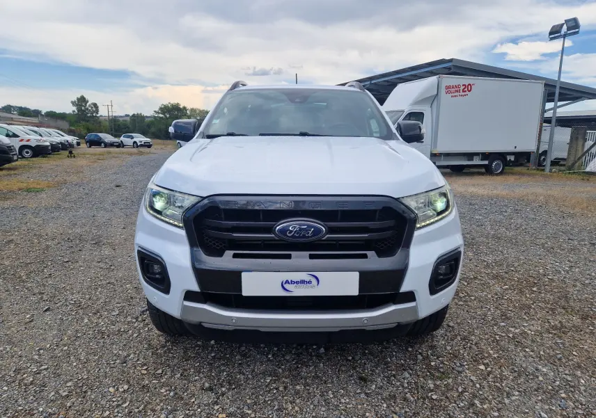 Vue avant d'un Ford Ranger Super Cabine blanc 4x4 avec calandre noire et phares allumés sur un terrain extérieur.