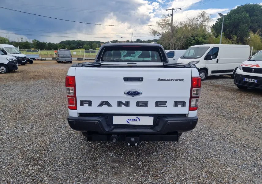 Vue arrière du Ford Ranger Wildtrak blanc avec benne ouverte et attelage visible sur un parking extérieur.