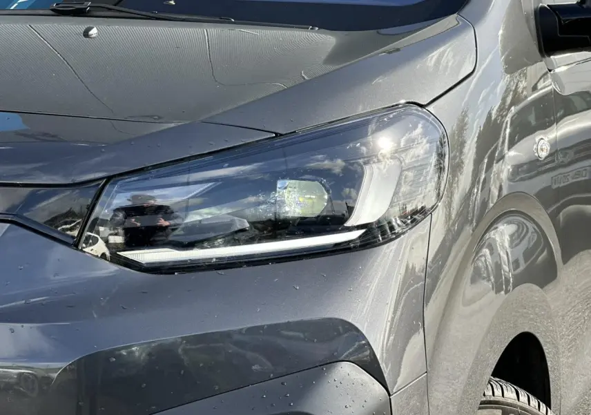 Gros plan sur le phare avant droit du FIAT Scudo Fourgon gris Platinium avec carrosserie lisse et reflets lumineux.