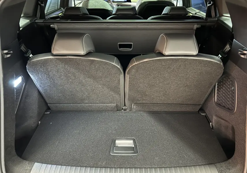 Vue du coffre arrière du Peugeot 5008 III Hybrid 145 e-DCS6 GT, intérieur noir avec sièges rabattus partiellement visibles.